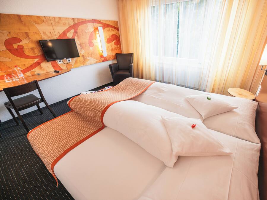 A hotel room with a bed, a desk, a chair, a TV, and a window with curtains.