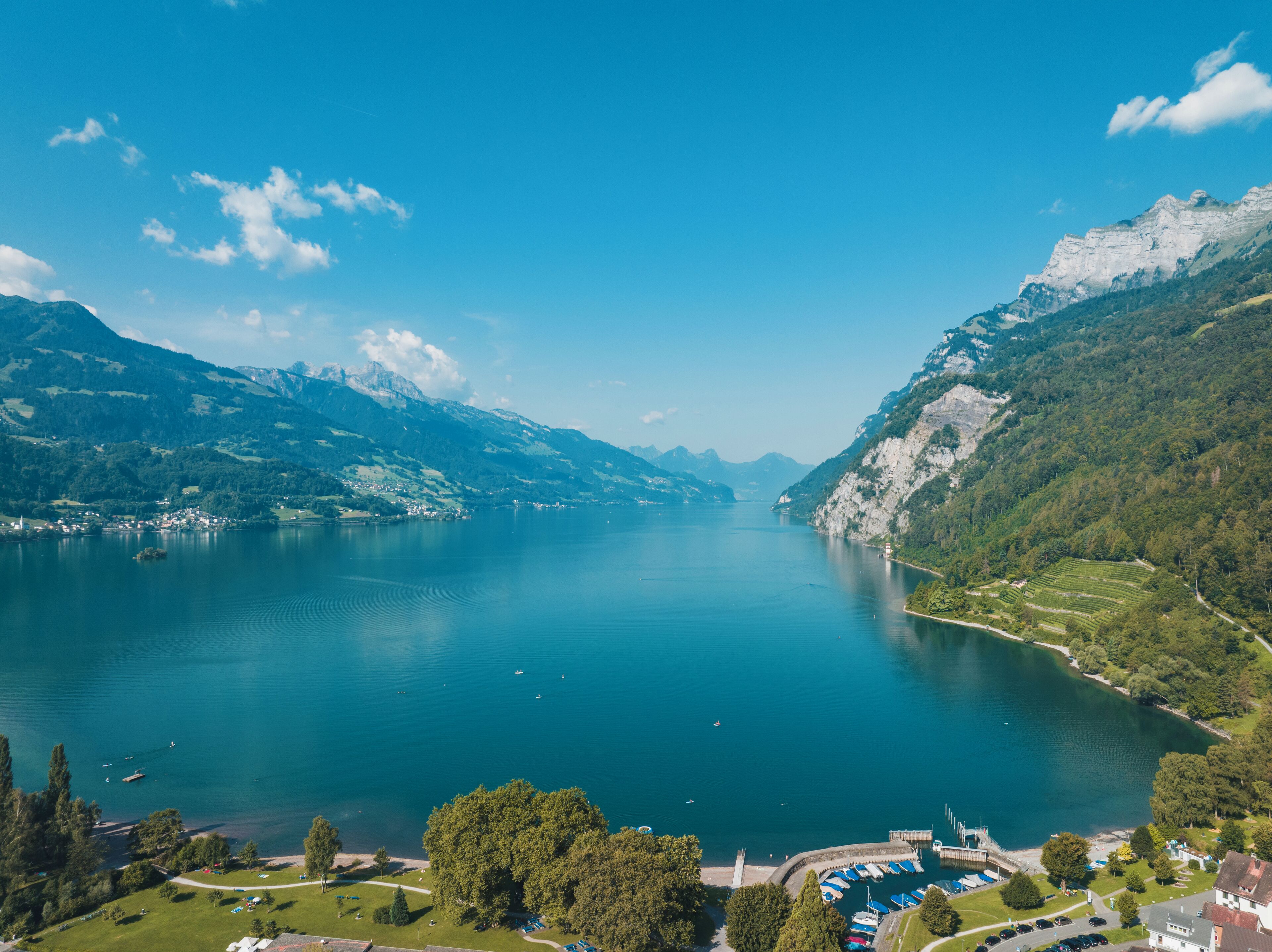 Vista panoràmica d'un llac envoltat de muntanyes, amb un petit poble i cel serè.