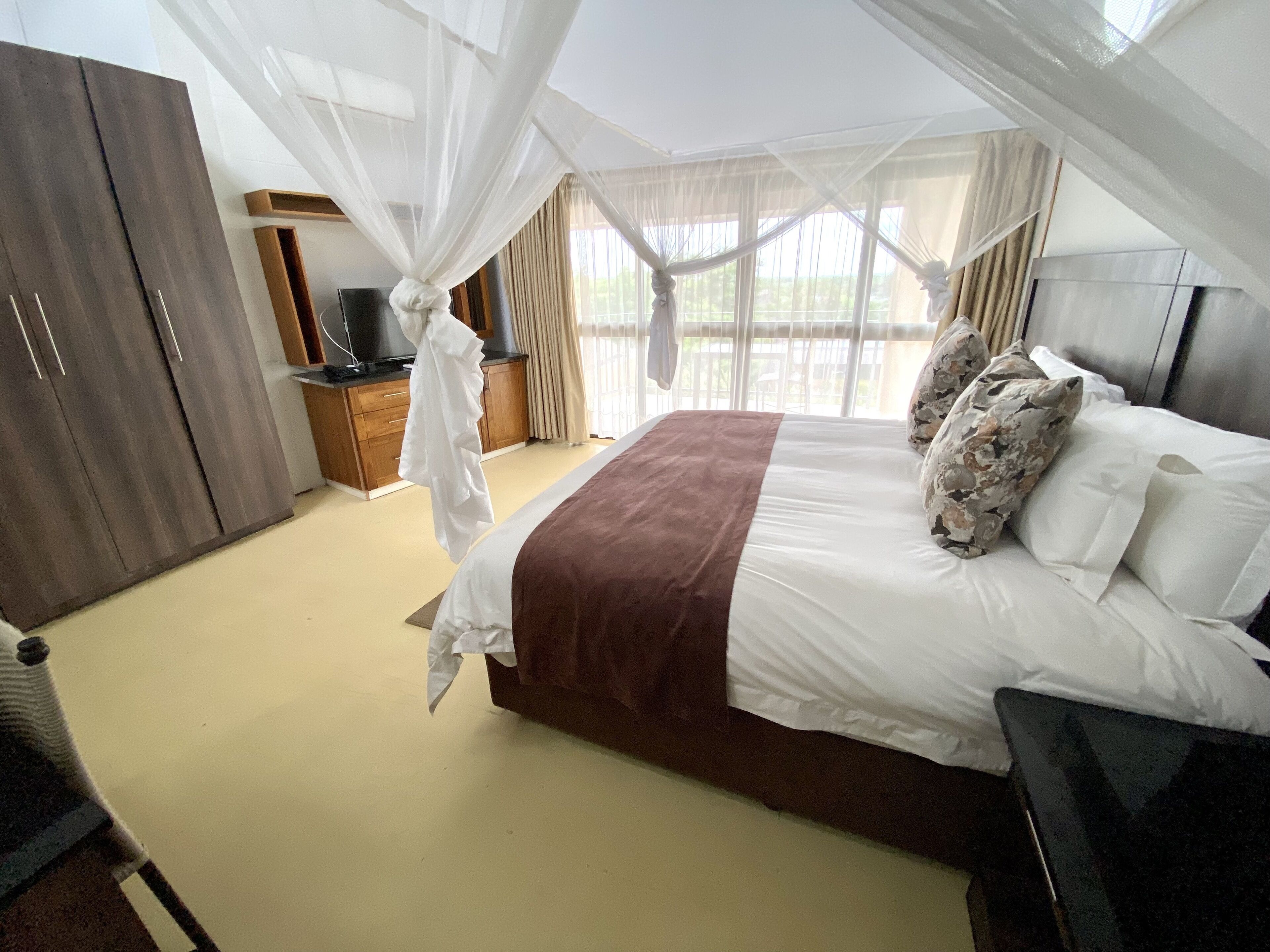 Une chambre à coucher avec un lit, une armoire, une télévision et une fenêtre avec des rideaux.