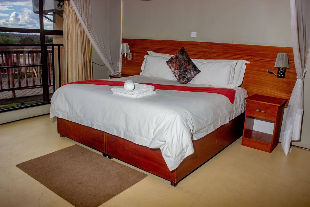 Ein großes Bett mit weißen Leinen, ein Holzkopfstück, ein Nachttisch und Blick ins Freie.