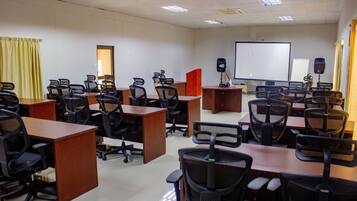 Uma sala de conferências com várias mesas e cadeiras, um quadro branco e uma tela de projeção.