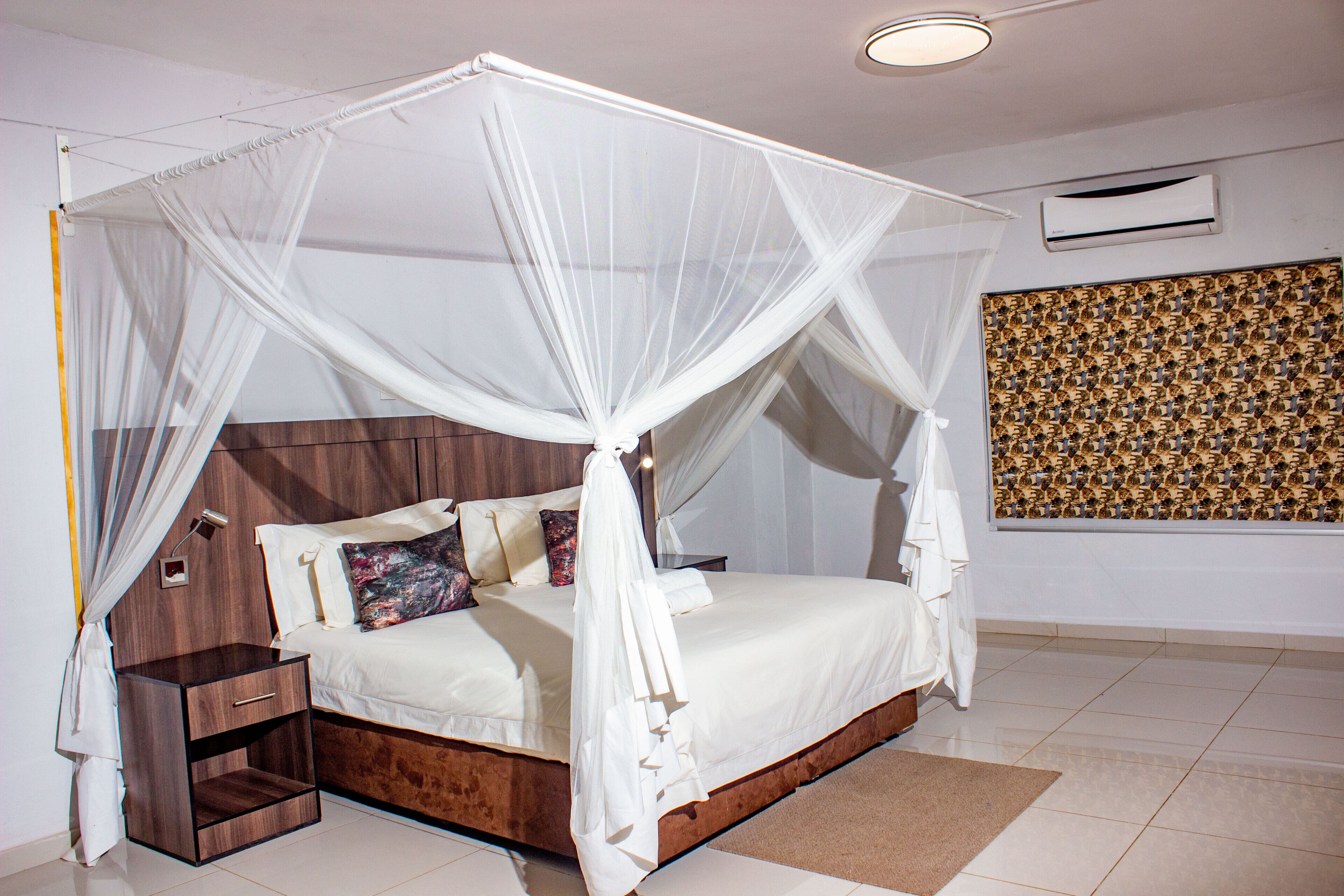 A bedroom with a four-poster bed, a bedside table, and a wall-mounted air conditioner.
