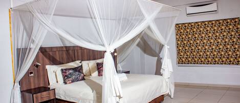 A bedroom with a four-poster bed, a bedside table, and a wall-mounted air conditioner.