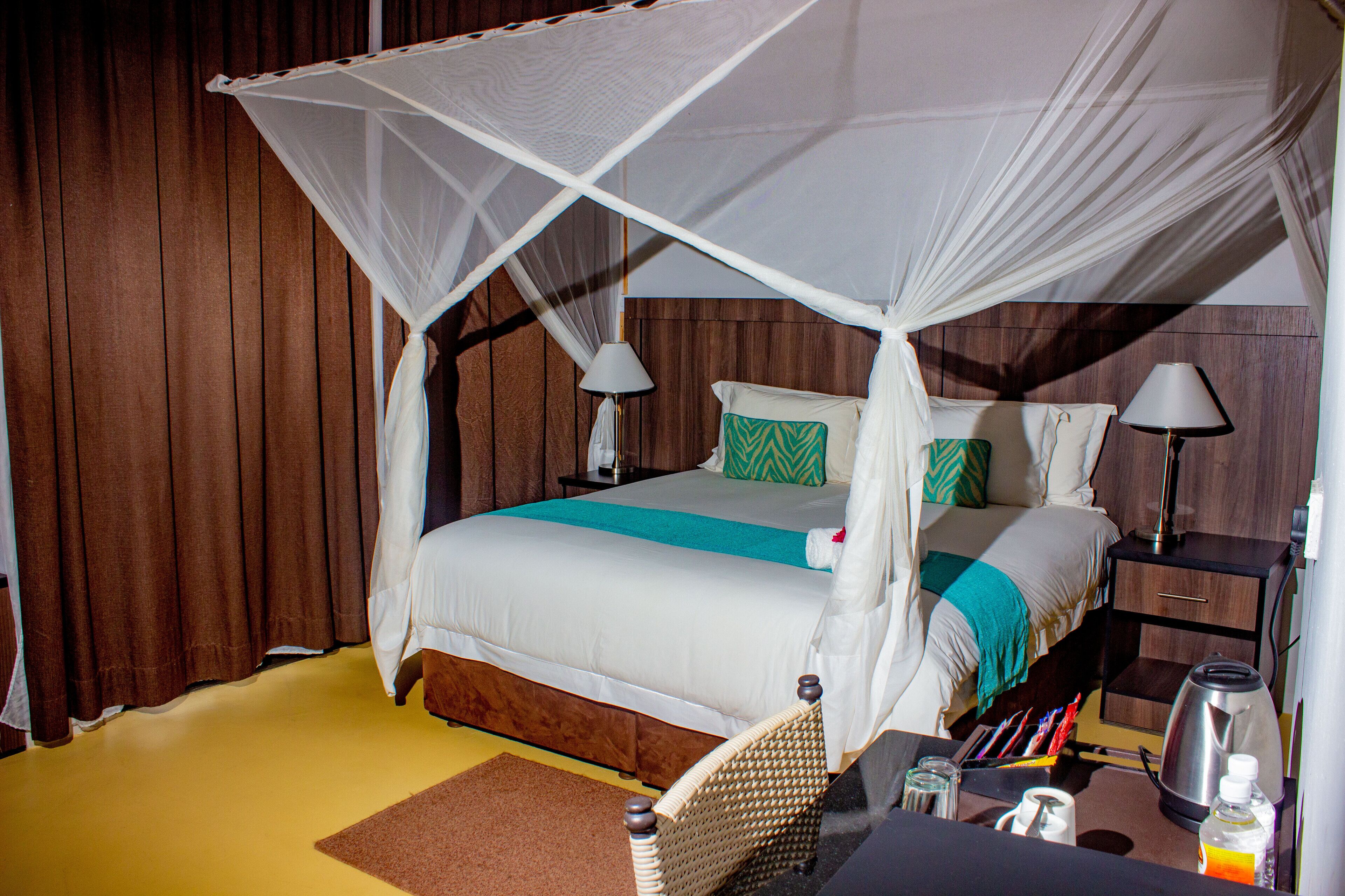 A bed with a canopy, bedside lamps, a nightstand, and a coffee pot.