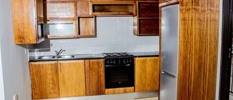 A kitchen with wooden cabinets, a stainless steel sink, a stove, and a refrigerator.
