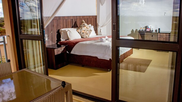 Un dormitorio con cama, mesita de noche y puerta de vidrio que da a un espacio exterior.