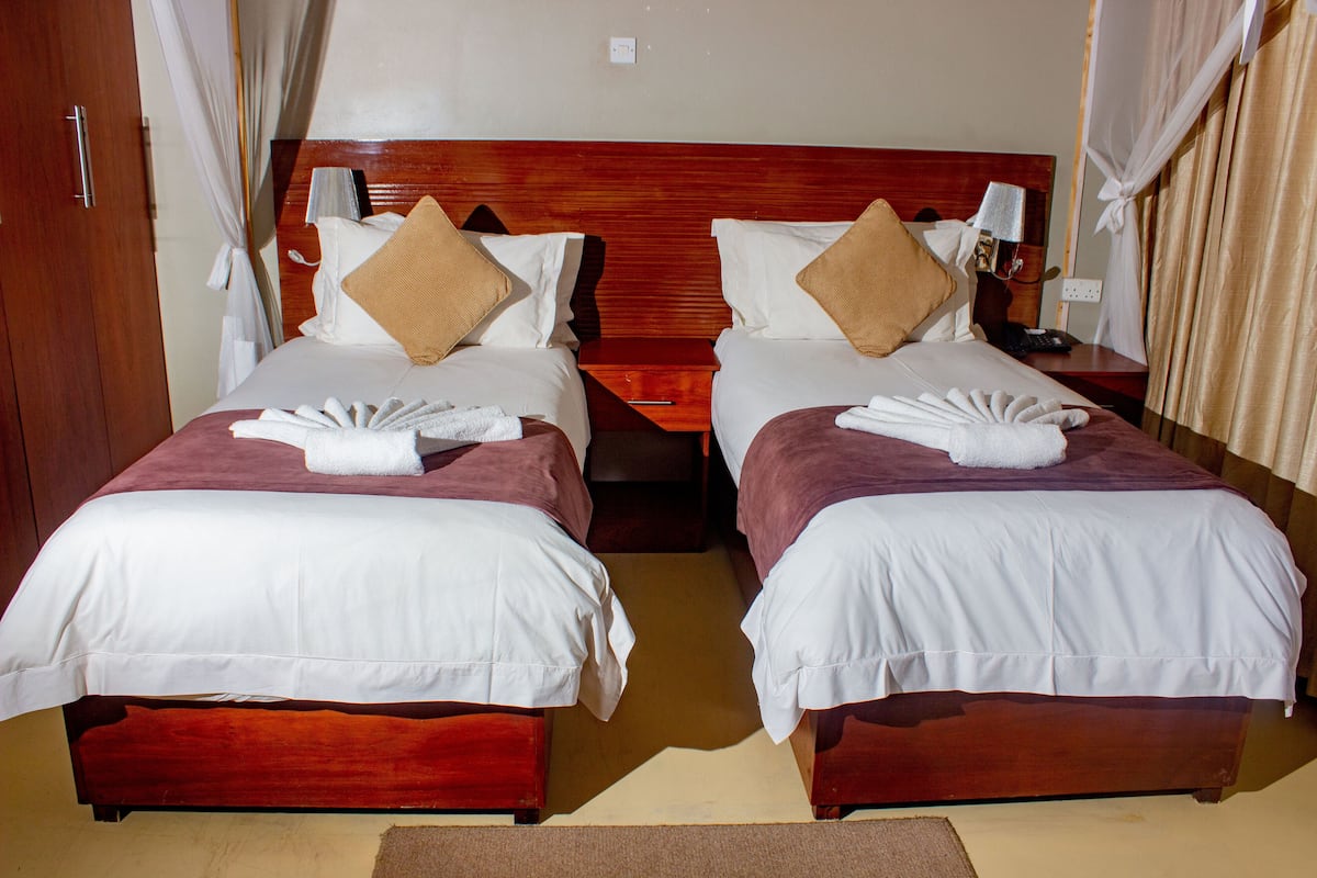 Ein Doppelzimmer mit zwei Betten, jeweils mit Holz Kopfteil, weißen Bettwäsche und braunen Kissen. An jedem Bett befindet sich ein Nachttisch mit Lampe und Telefon.