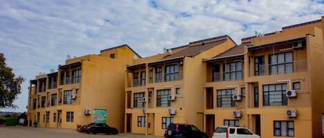 A multi-story building with a yellow facade, multiple balconies, and several parked cars.
