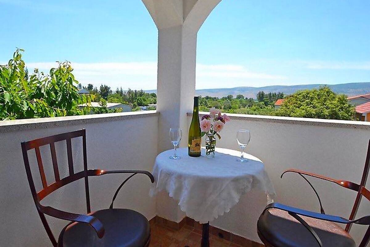 A balcony with a table set for two, a bottle of wine, and a vase with flowers.