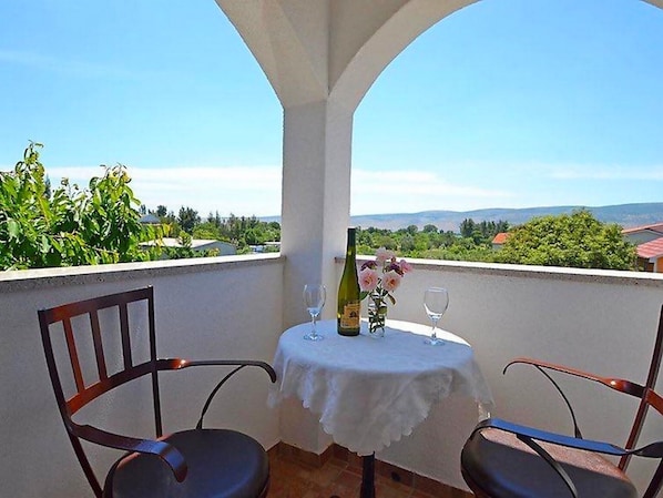 A balcony with a table set for two, a bottle of wine, and a vase with flowers.