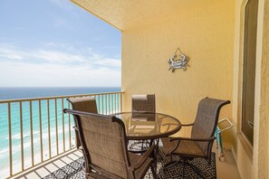 Un balcon avec une table et des chaises en verre, un élément décoratif mural et une vue sur l’océan.