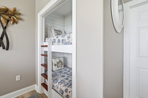 A bunk bed with patterned bedding, a decorative wall plant, and a white door.