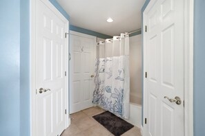 Une salle de bain avec des portes blanches, un rideau de douche à motifs marins et un tapis foncé sur le sol.