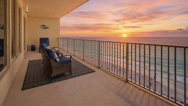 A balcony with a view of the ocean at sunset, a wicker chair, and a patterned rug. - Relaxing Beachfront Condo with Beach Access - Unit 1603 by RedAwning (Panama City Beach)
