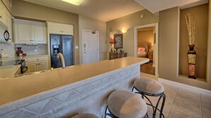 A kitchen with a central island, bar stools, and a refrigerator. - Roomy Oceanfront Condo with Breathtaking View and Beachside Pool - Unit 1906 by RedAwning (Panama City Beach)