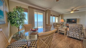 A spacious living room with a glass dining table, wicker chairs, a large potted plant, and a television. - Roomy Oceanfront Condo with Breathtaking View and Beachside Pool - Unit 1906 by RedAwning (Panama City Beach)