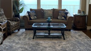 A living room with a sofa, armchair, and coffee table, large windows with a view of the ocean, and a ceiling fan. - Roomy Oceanfront Condo with Breathtaking View and Beachside Pool - Unit 1906 by RedAwning (Panama City Beach)