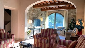 A cozy living room with striped sofas, a glass coffee table, and a stone wall. - Villa Pie Vecchia in Chianti (Greve in Chianti)