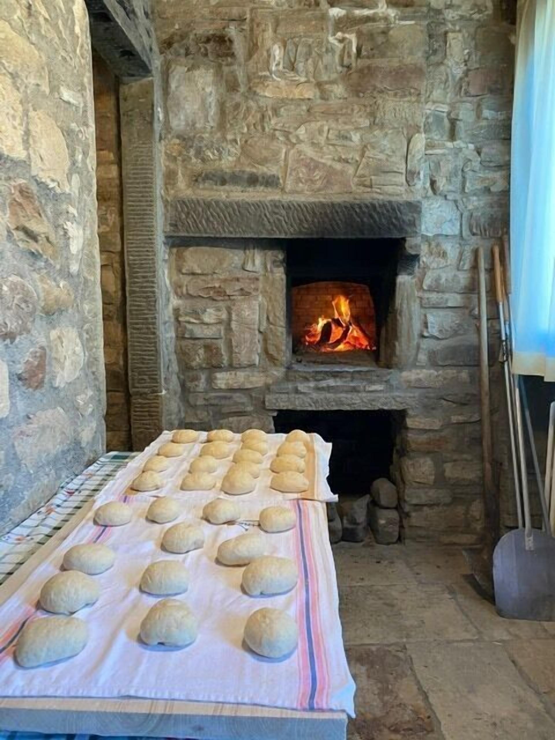 A stone fireplace with a fire, a table with dough balls, and a rustic stone wall.