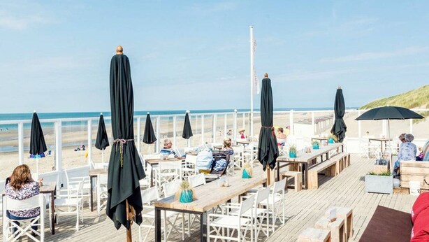 A beachside restaurant with outdoor seating, tables, and umbrellas.