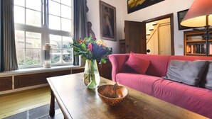 A living room with a pink sofa, a wooden coffee table, a vase with flowers, and a bookshelf.