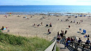 A beach with people, tents, and a wooden boardwalk leading to the water.