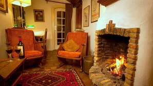 A cozy room with a stone fireplace, two wooden chairs, a table with wine glasses, and a patterned rug.