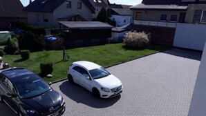 Eine Auffahrt mit zwei parkenden Autos, ein weißes Auto im Vordergrund und ein schwarzes Auto im Hintergrund.