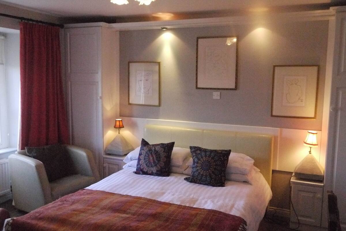 Une chambre d’hôtel comprenant un lit, deux tables de chevet, une chaise et trois œuvres d’art encadrées accrochées au mur.