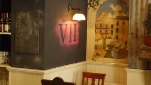 A bar area with a dark wall, a 'VII' illuminated sign, a mural, and a wooden chair. - 7 Houses (Armagh)