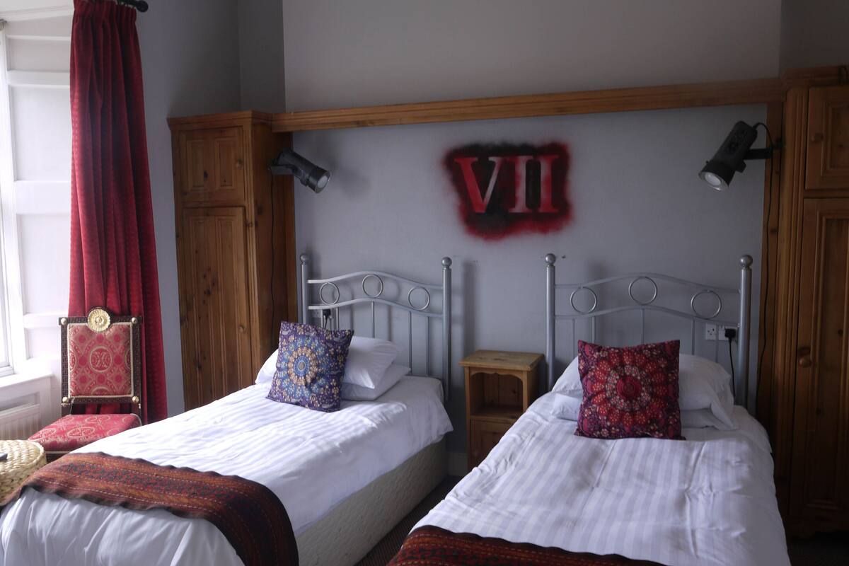 Une chambre avec deux lits simples, une armoire en bois, un rideau rouge et un luminaire fixé au mur.