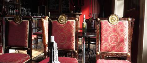 A bar area with red upholstered chairs, a bottle on the table, and a menu on the wall.