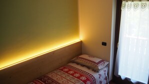 A small, cozy room with a single bed, a bedside table, and a window with a curtain. - KALIPE' DOLOMITI Appartment (LONGARONE (BL))