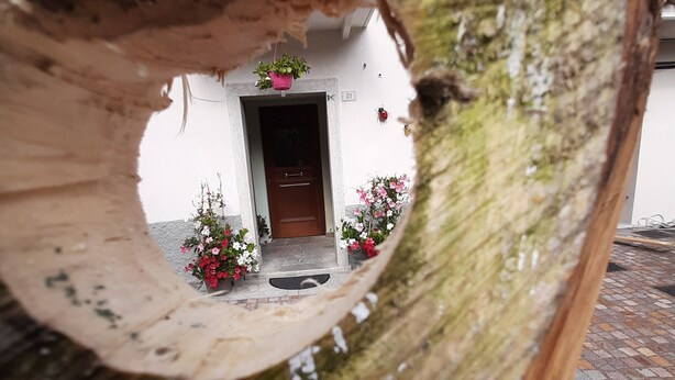 A wooden structure with a circular opening, through which a building entrance and potted plants are visible. - KALIPE' DOLOMITI Appartment (LONGARONE (BL))