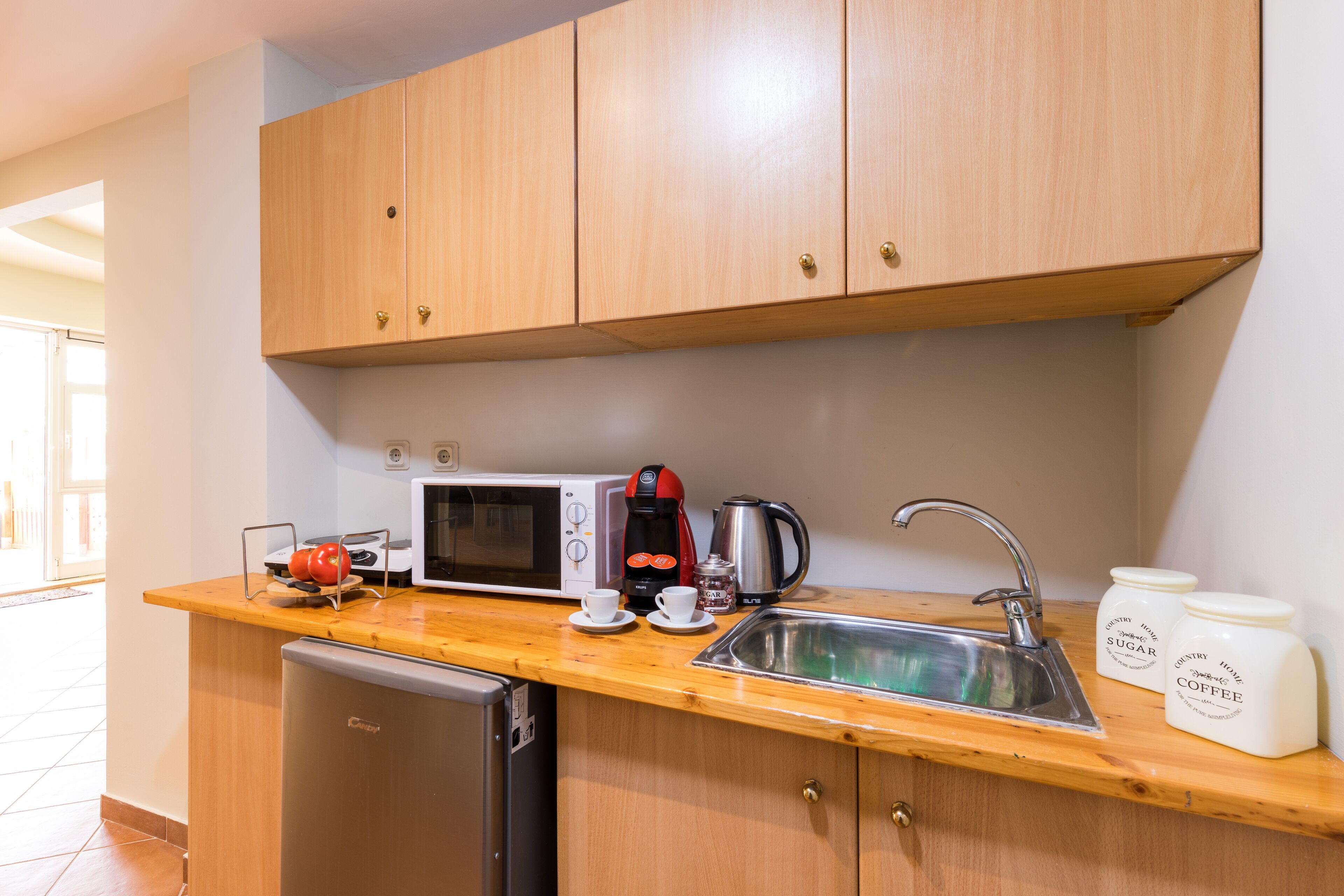 Eine kompakte Küche mit Holzausstattung, einer Mikrowelle, einer Kaffeemaschine, einem Spülbecken und einem Kühlschrank.