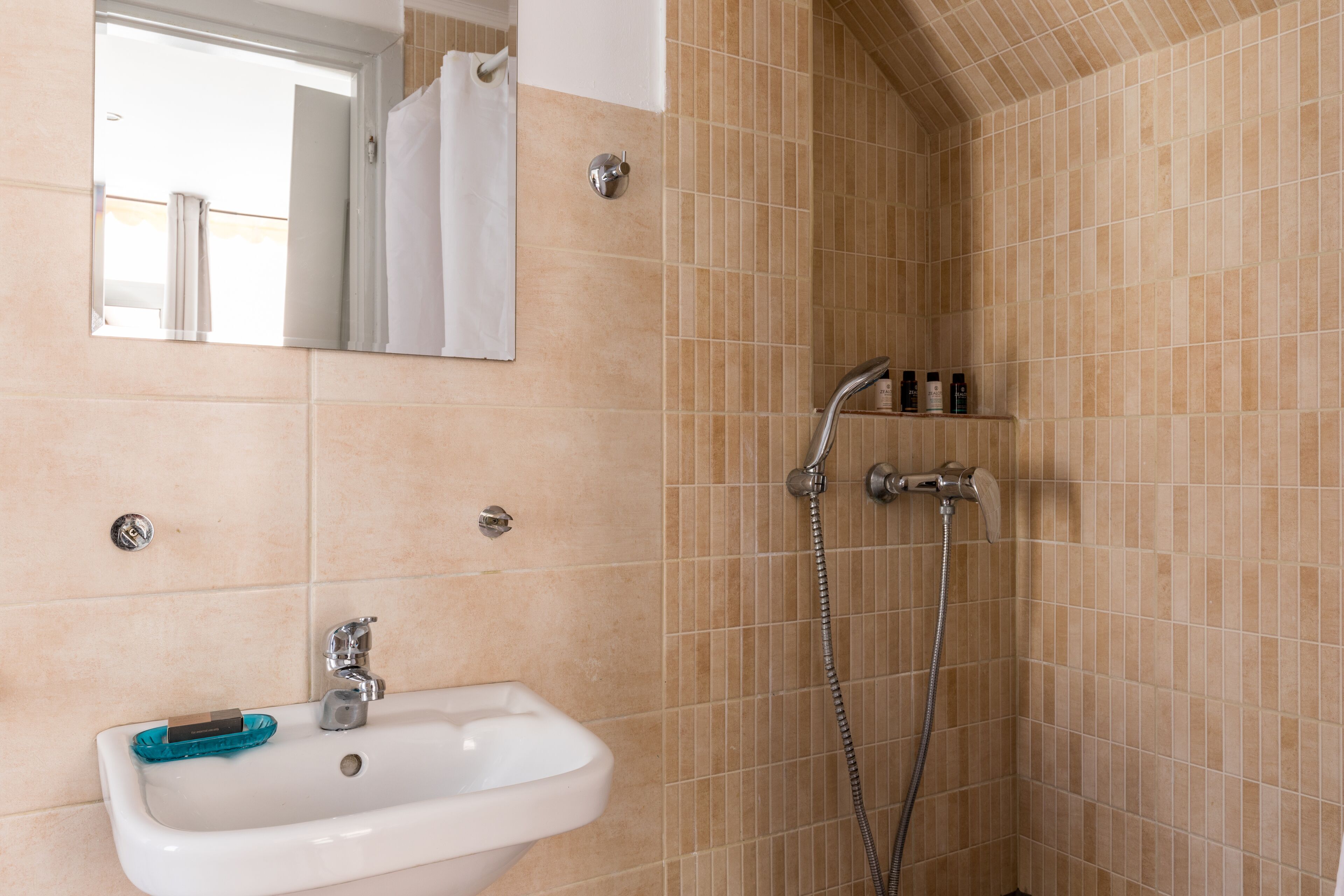 A bathroom with a sink, mirror, shower, and tiled walls.