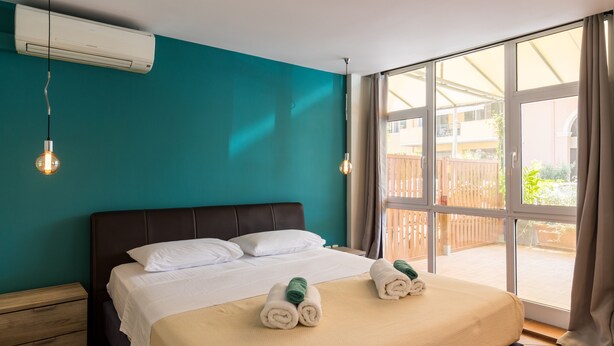 Habitación de hotel con una cama grande, paredes color turquesa y vistas al exterior.