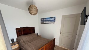 A bedroom with a wooden bed, a bedside table, a lamp, a painting on the wall, and a door. - Charming apartment in a family house with sea view in Damgan (Damgan)