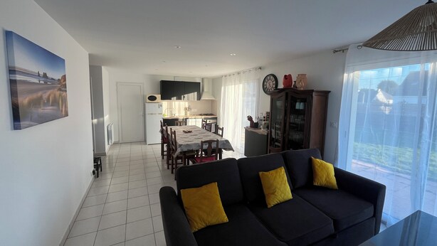 A modern living room with a black sofa and yellow cushions, a dining area with a table and chairs, and a kitchen with white cabinets and a black microwave. - Charming apartment in a family house with sea view in Damgan (Damgan)