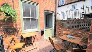 A brick patio with wooden furniture, including a table and chairs, and a hanging plant. - 2 Bedroom City Centre Cottage set in a Private Courtyard (Canterbury)