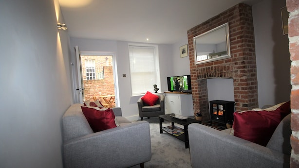 A living room with two grey sofas, a red cushion, a black coffee table, a fireplace, and a television. - 2 Bedroom City Centre Cottage set in a Private Courtyard (Canterbury)