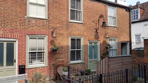 A two-story brick house with multiple windows, a front door, and a small garden area with a bench and potted plants. - 2 Bedroom City Centre Cottage set in a Private Courtyard (Canterbury)