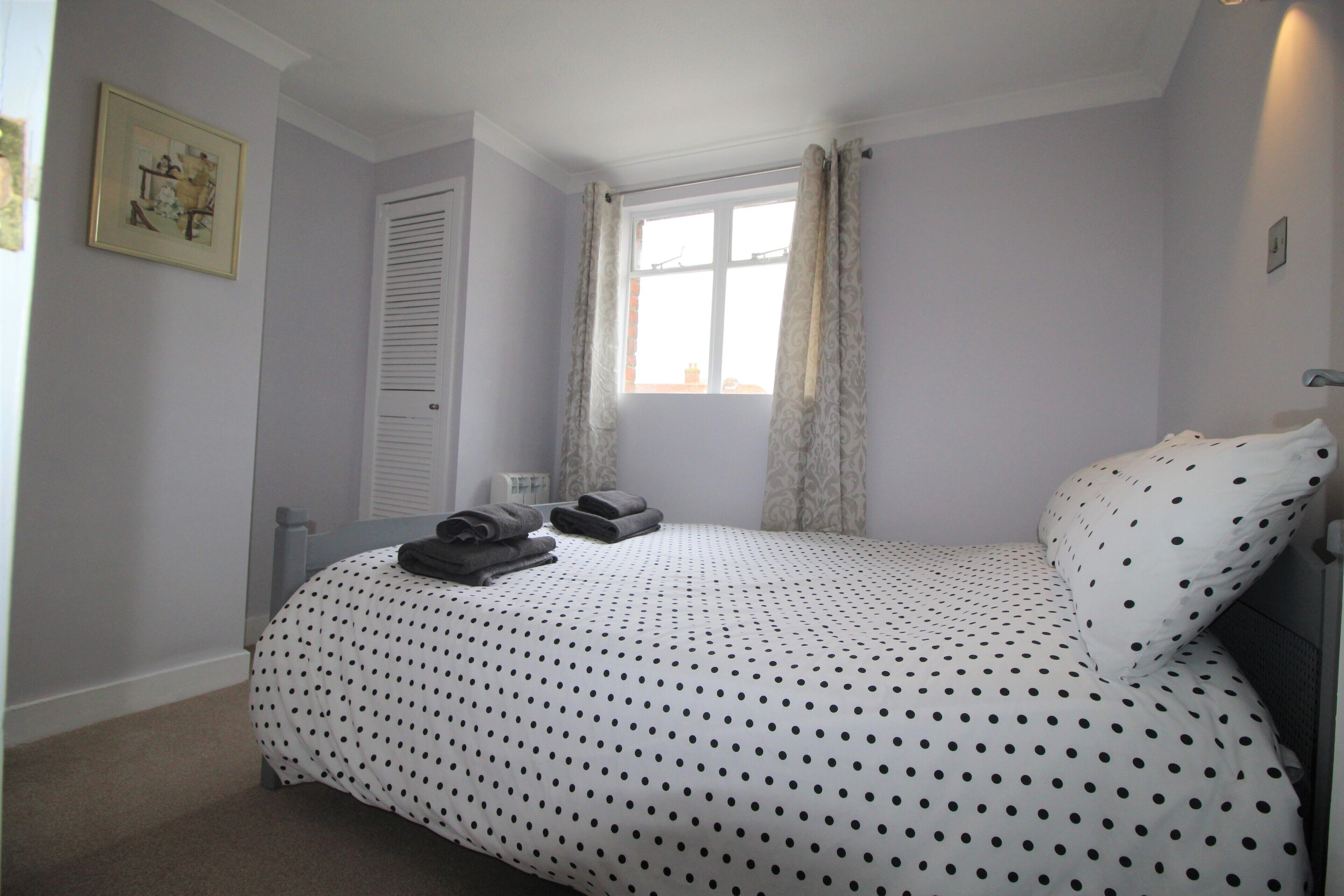 A bedroom with a bed, a window with curtains, a door, and a framed picture on the wall.