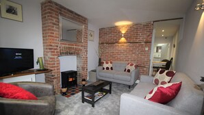A living room with a brick fireplace, a sofa, a coffee table, and a television. - 2 Bedroom City Centre Cottage set in a Private Courtyard (Canterbury)