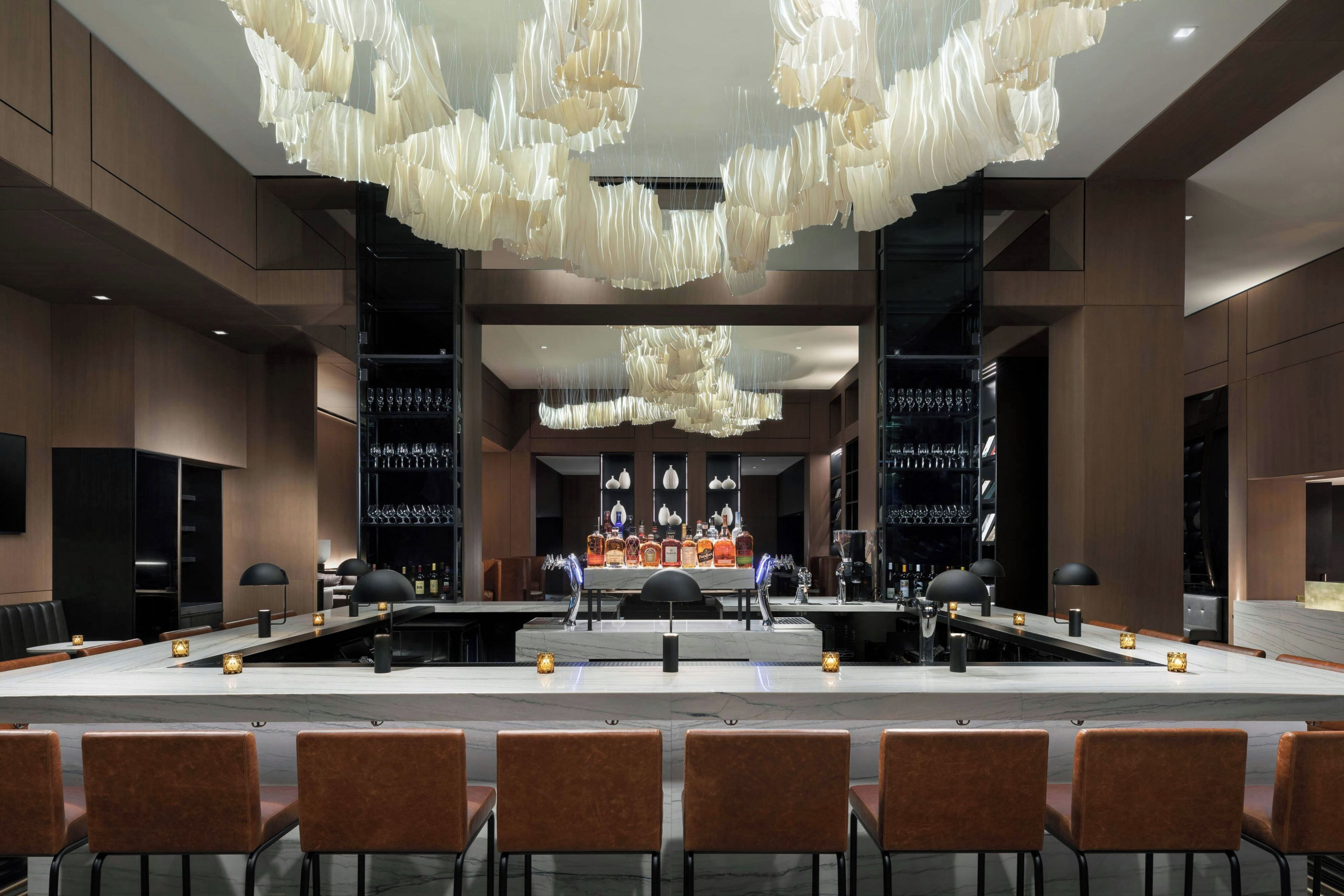 A modern bar area with a marble countertop, bar stools, and a central bar station.