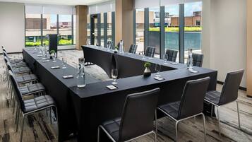 A conference room with a long table, chairs, and a view of buildings through large windows.