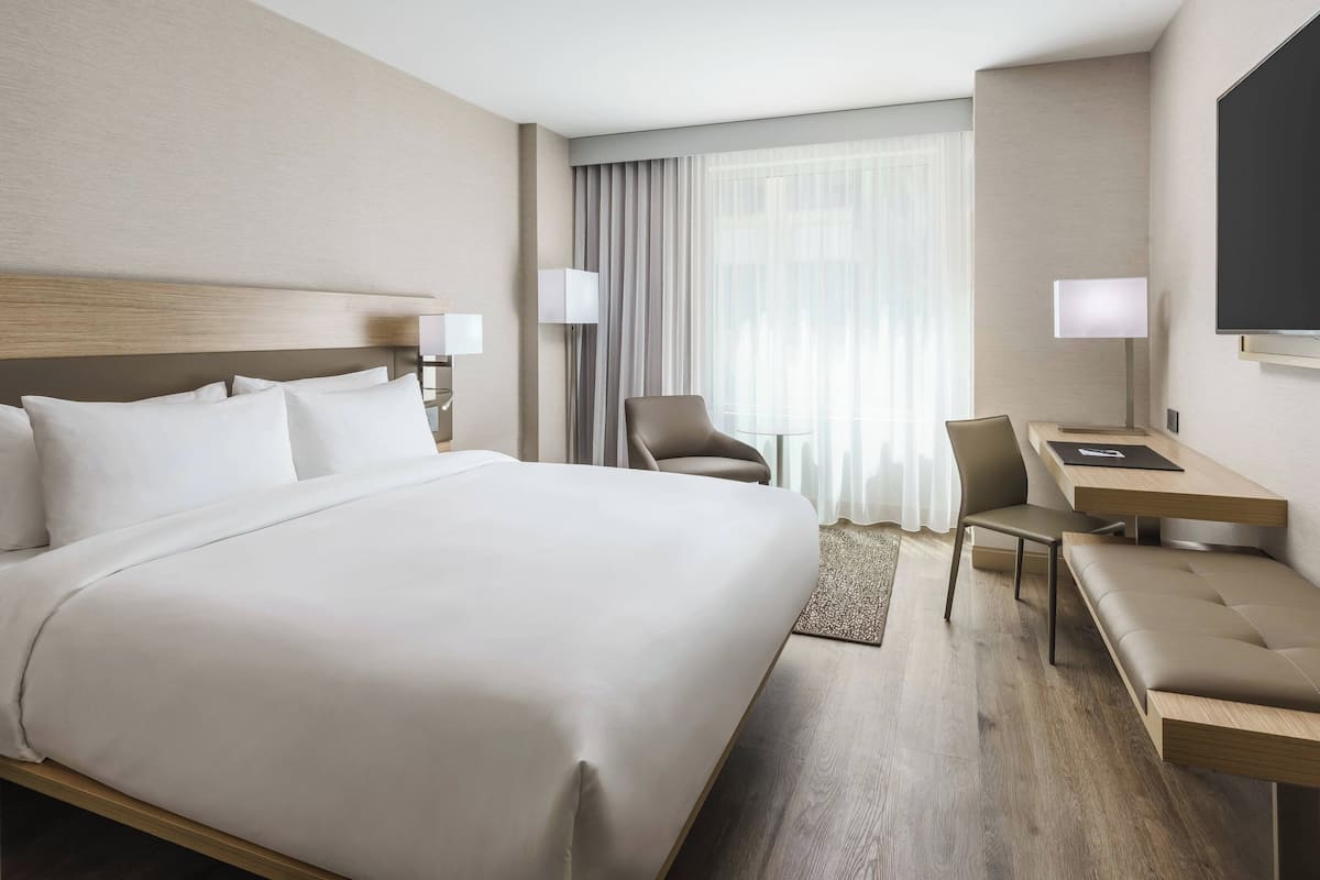 A modern hotel room with a large bed, a desk, a chair, and a TV.