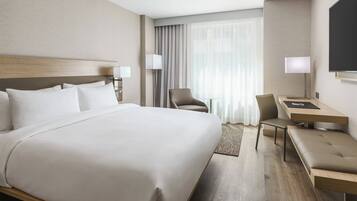 A modern hotel room with a large bed, a desk, a chair, and a TV.