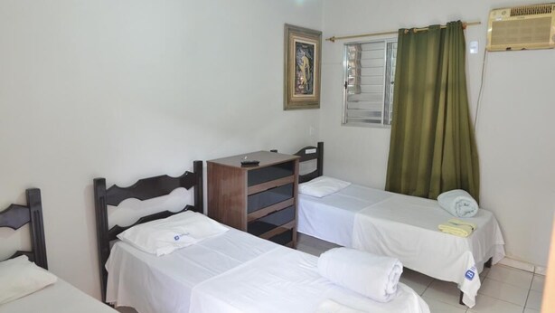 Habitació d'hotel amb dos llits individuals, un taulell de nit de fusta, un quadre amb marc a la paret i una finestra amb cortines verdes.