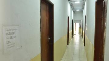 Corredor com portas em ambos os lados, um aviso solicitando silêncio e piso de azulejos.